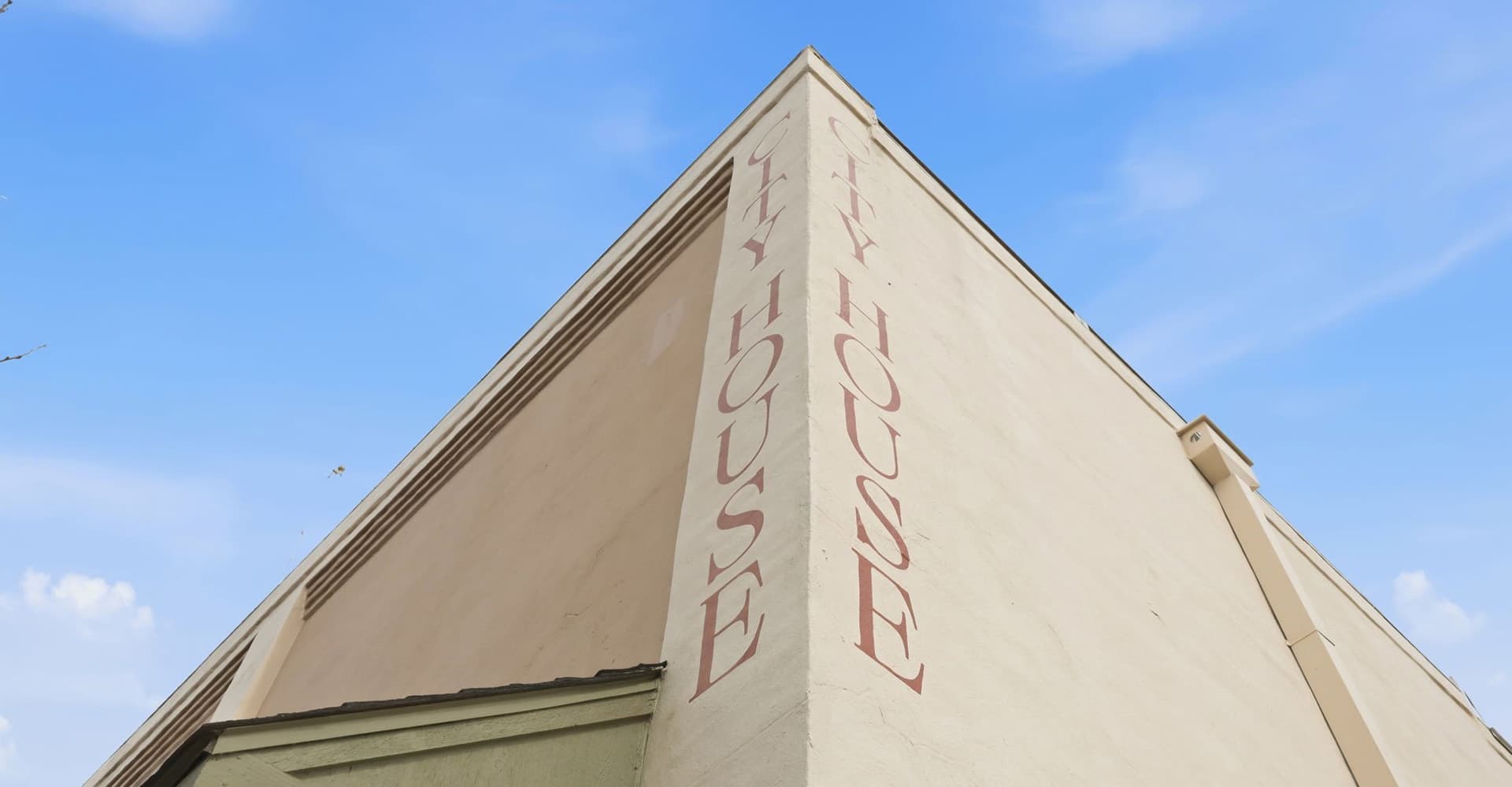 A close-up of a building corner with "FLY HOUSE" painted on the side against a blue sky.